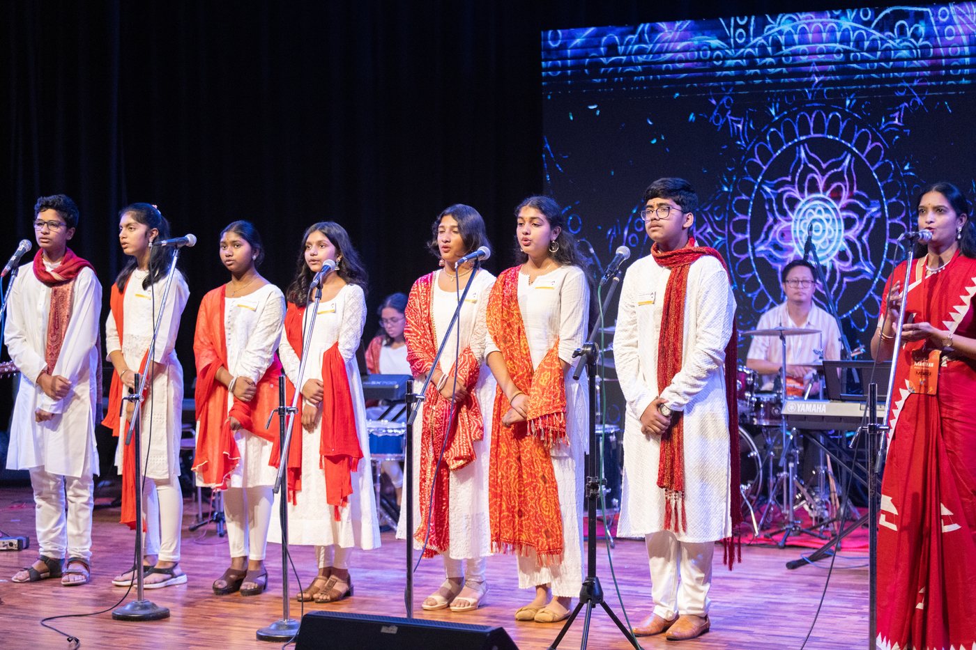 A vocal ensemble in red and white clothing singing into microphones on stage.