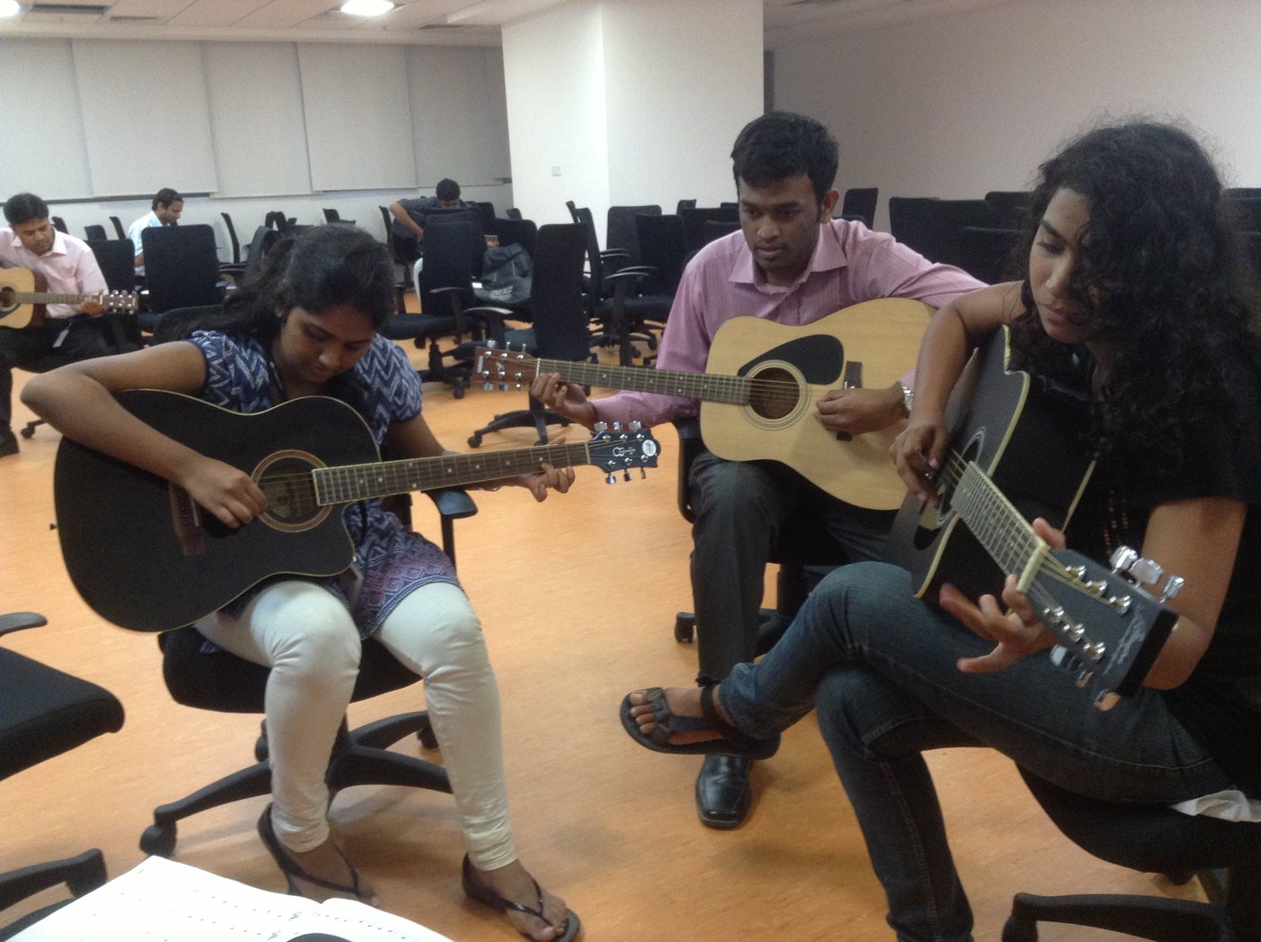 Three learners seated in a classroom practising acoustic guitar.