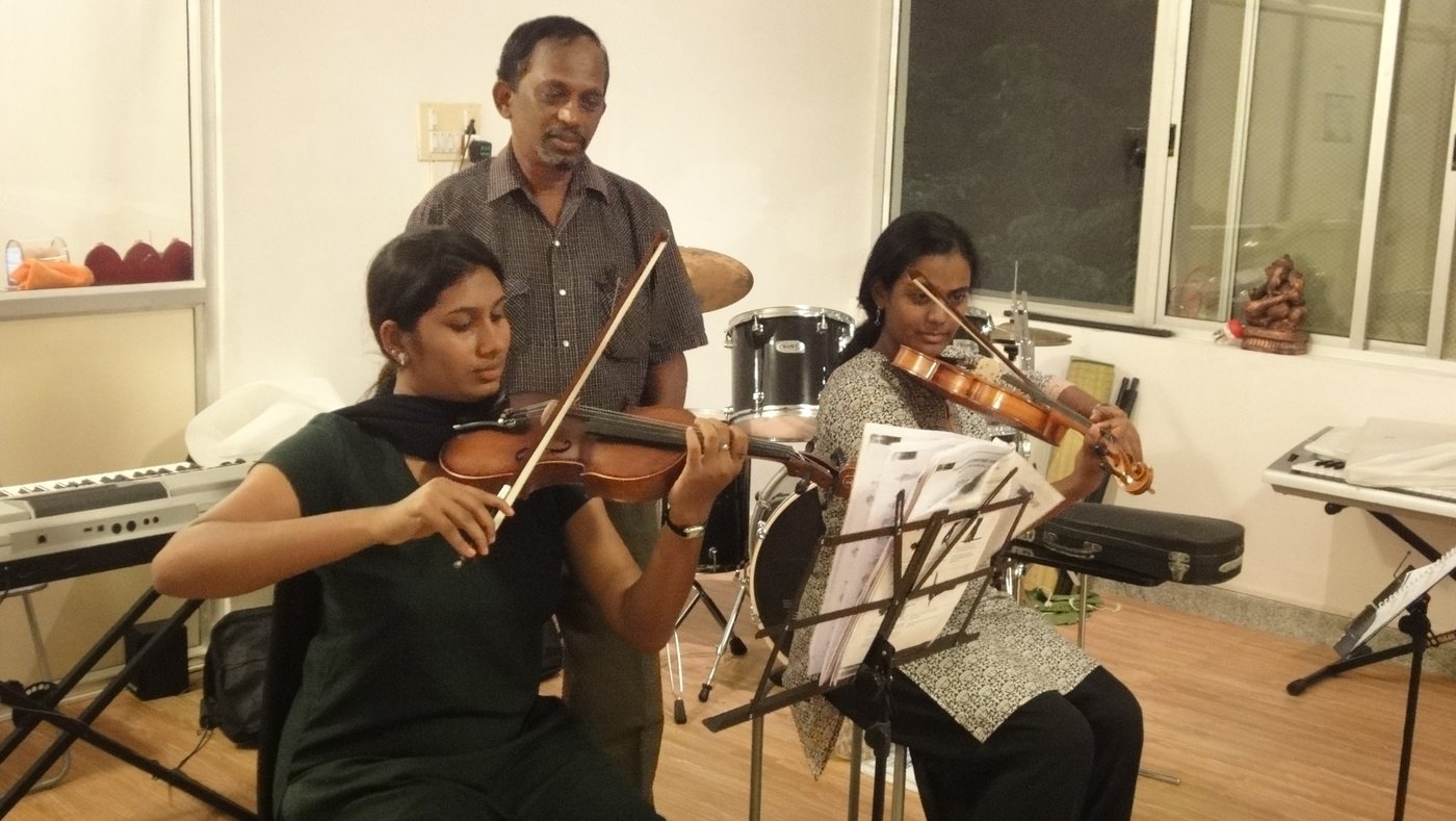 An instructor standing beside two learners playing violins and reading music.