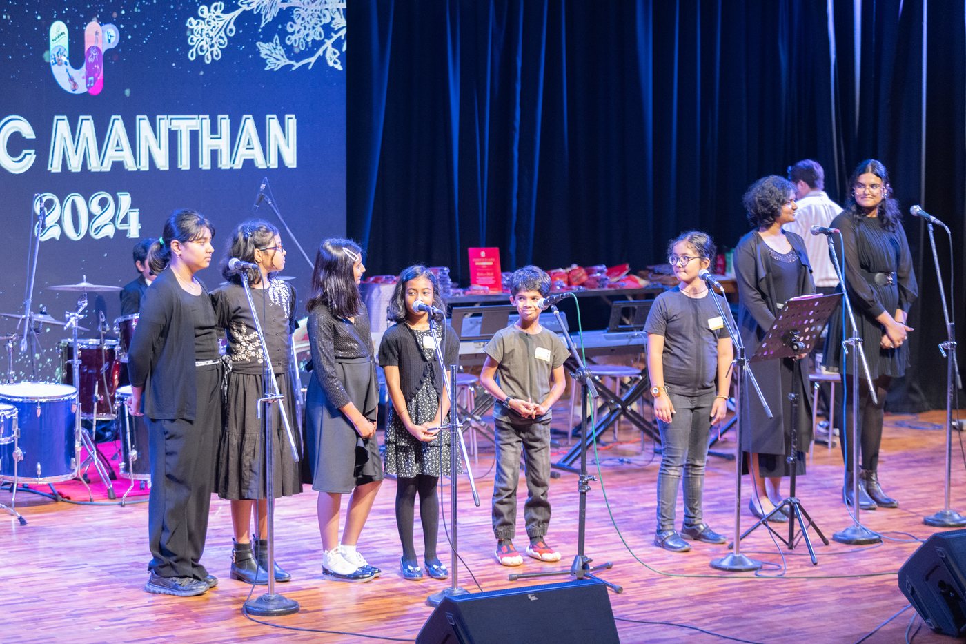 A group of singers at microphones on the Music Manthan stage.